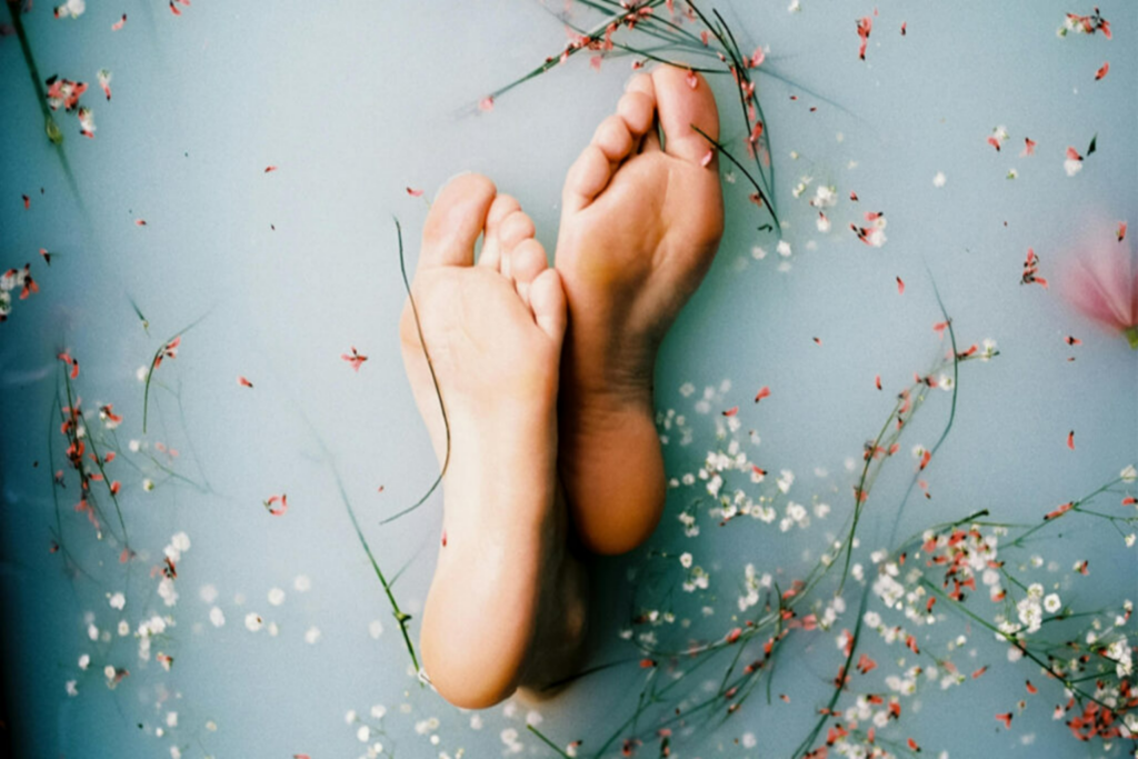 Plantas de los pies de una mujer rodeadas de flores en agua durante una sesión de bienestar