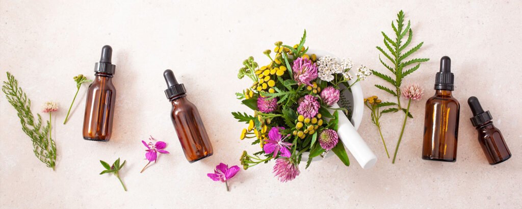 Cuatro botellas de esencias florales junto a un mortero blanco con flores frescas