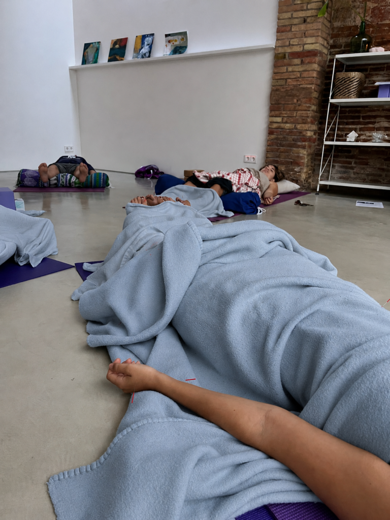 Personas recibiendo acupuntura comunitaria en esterillas de yoga, cubiertas con mantas.
